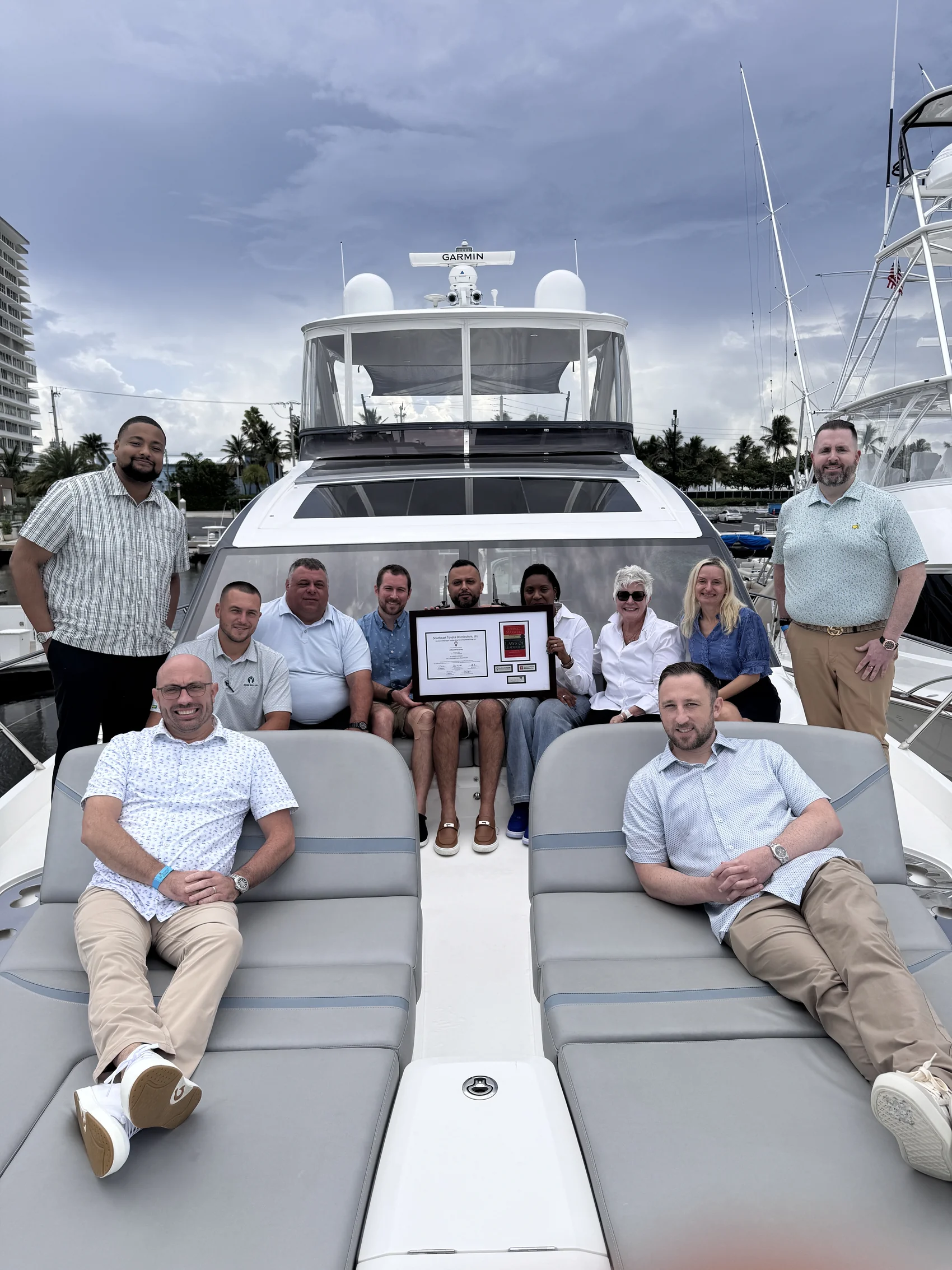 A dealership leadership team with Trish Buzzone, holding their Maxwell Leadership completion award on a yacht